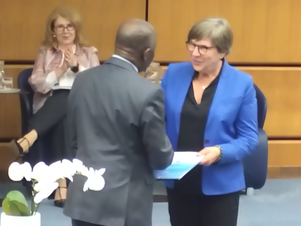 Après la signature, le Président de la HALC remet l'accord signé à une représentante de l'ONUDC, sous les applaudissements des autres délégués présents.
